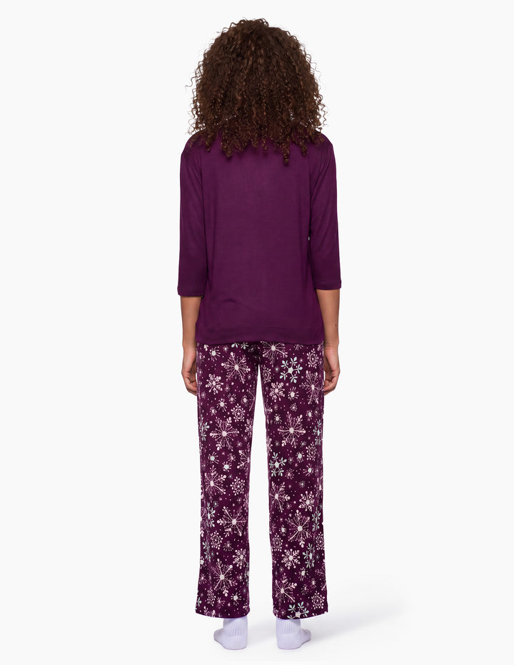A backside view of a model wearing a purple pajama top and matching purple snowflake pajama pants.