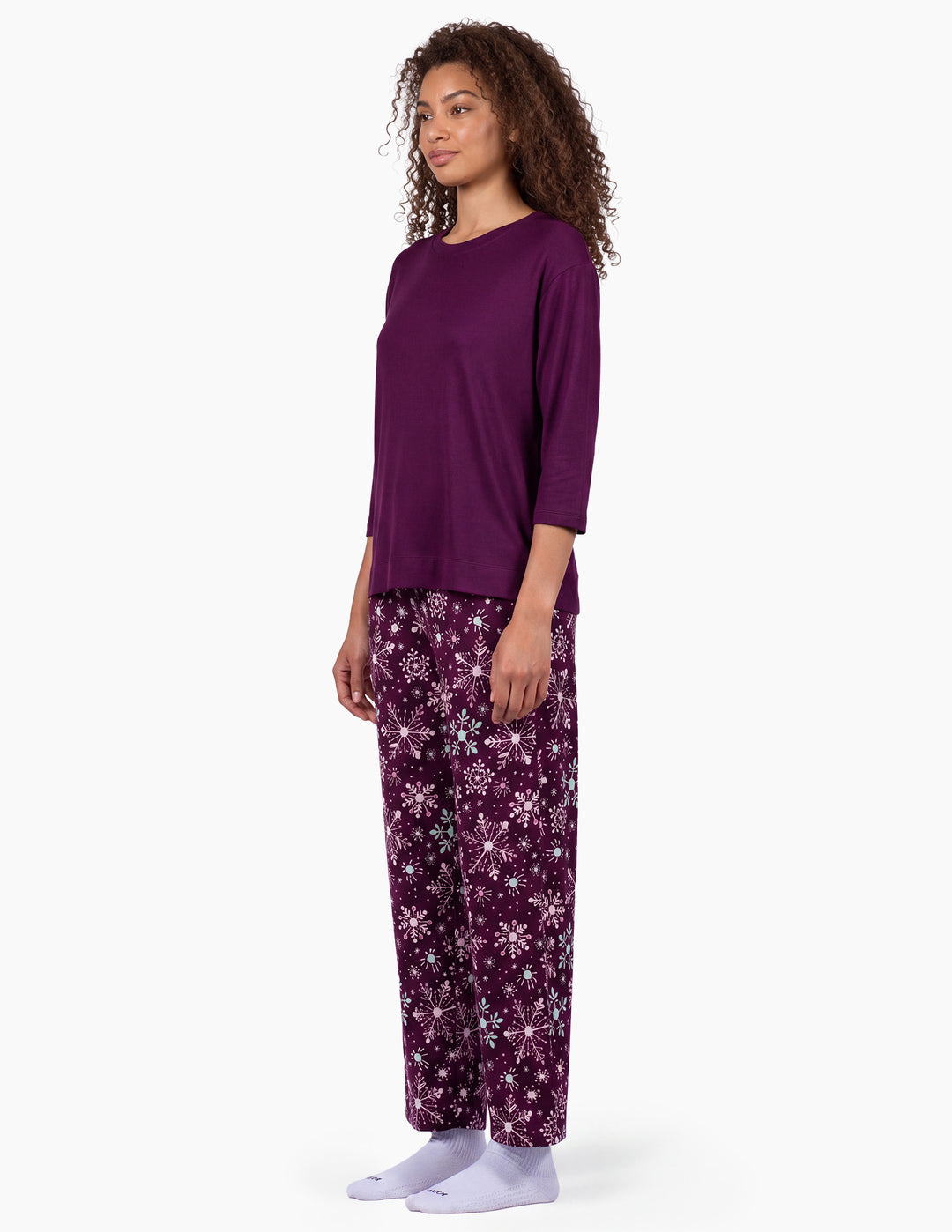 A sideview of a model wearing a purple pajama top and matching purple snowflake pajama pants.