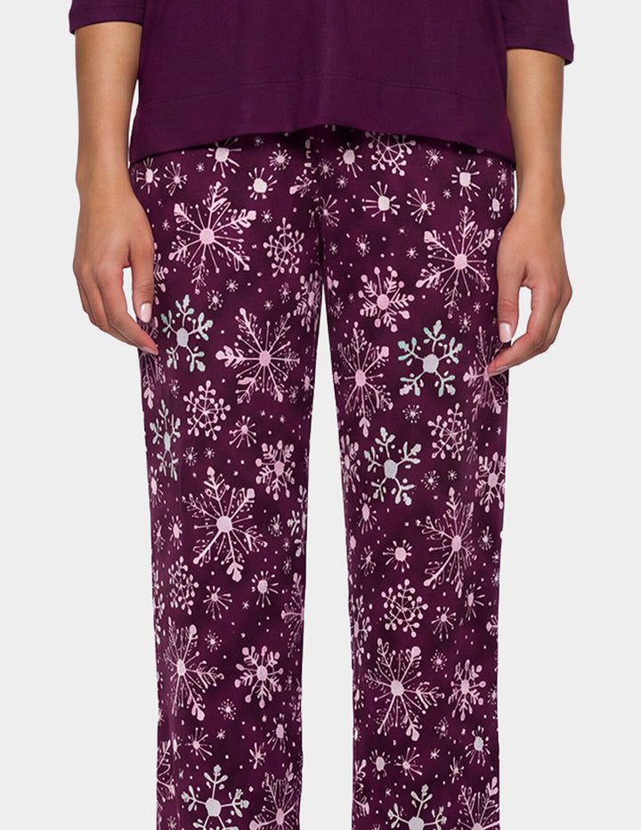 A model wearing a purple pajama top and snowflake pajama pants.