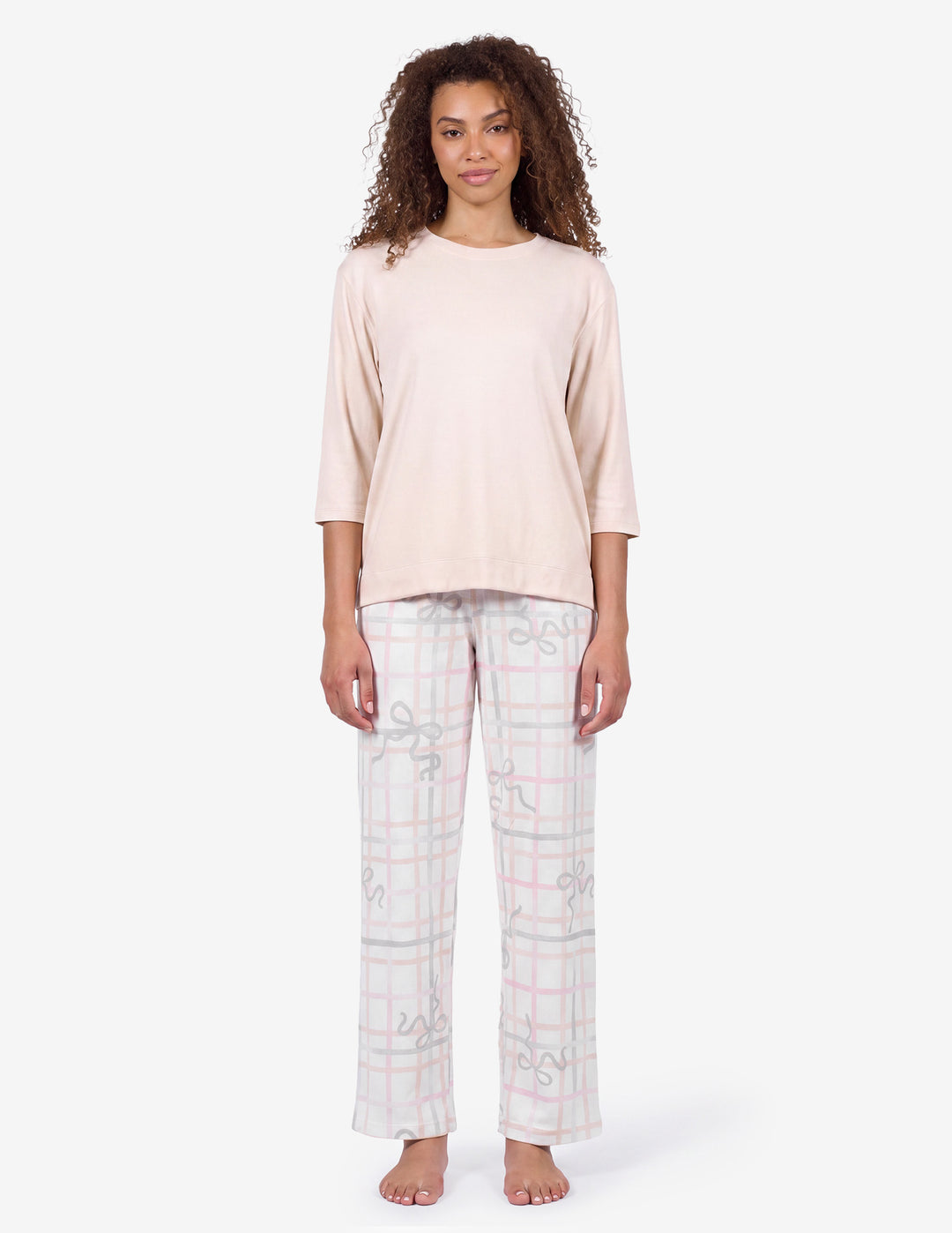 A model wearing a light pink pajama top and light gray pajama pants with a bow and stripe pattern against a light gray background.