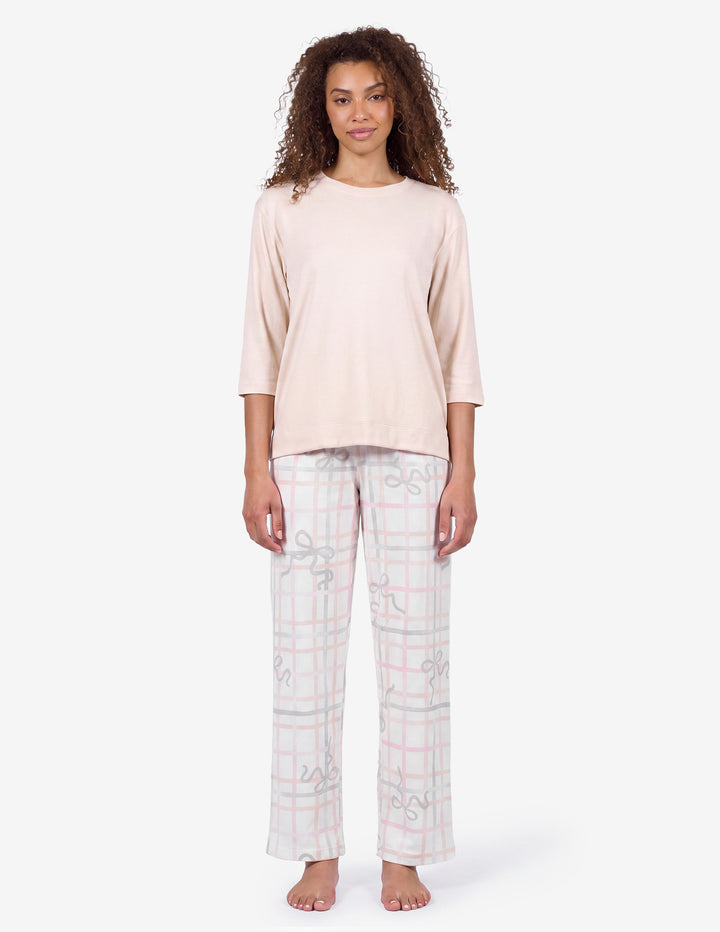 A model wearing a light pink pajama top and light gray pajama pants with a bow and stripe pattern against a light gray background.