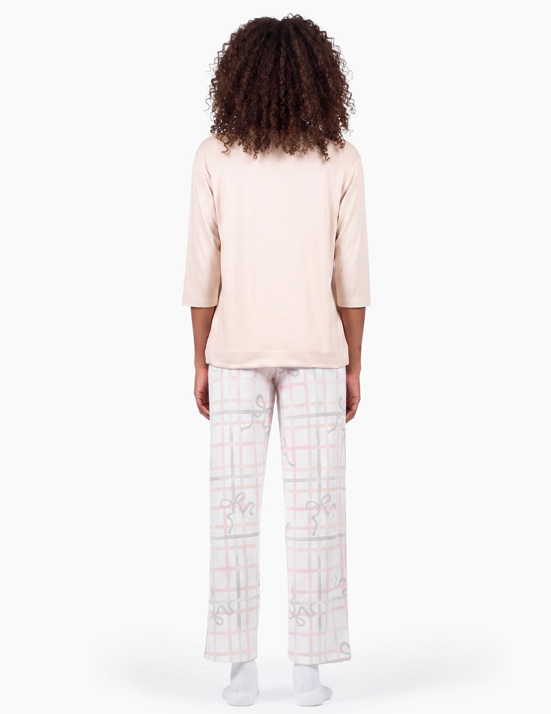 A backside view of a model wearing a light pink pajama top and light gray pajama pants with a bow and stripe pattern against a light gray background.