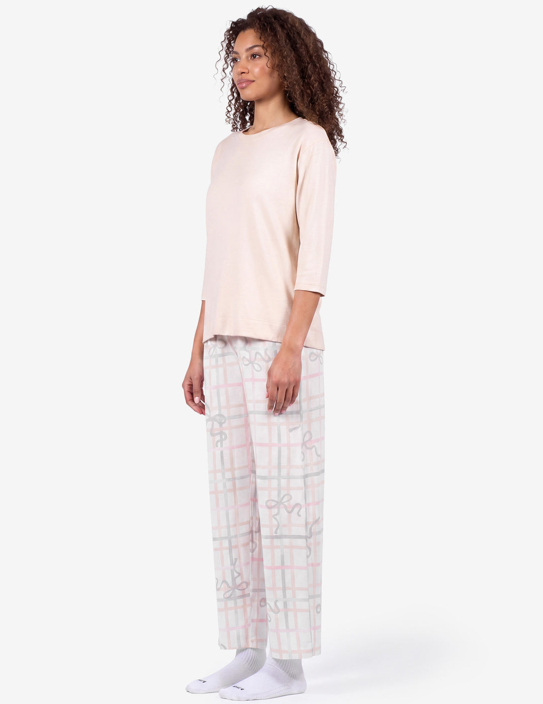 A sideview of a model wearing a light pink pajama top and light gray pajama pants with a bow and stripe pattern against a light gray background.