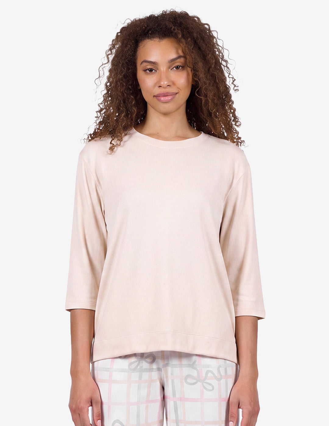 A close-up of a model wearing a light pink pajama top and light gray pajama pants with a bow and stripe pattern against a light gray background.