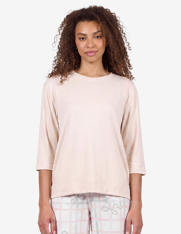 A close-up of a model wearing a light pink pajama top and light gray pajama pants with a bow and stripe pattern against a light gray background.