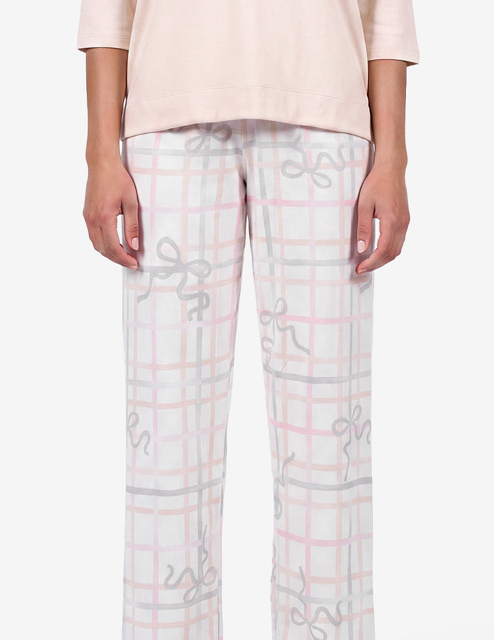 A model wearing a light pink pajama top and light gray pajama pants with a bow and stripe pattern against a light gray background.