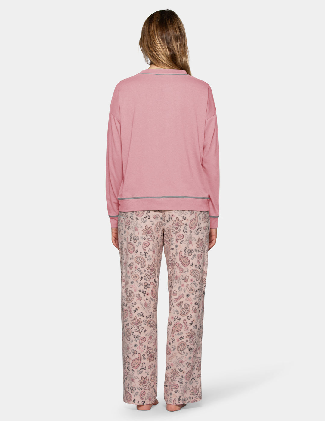 A backside view of a model wearing a pink long sleeve pajama top and patterned pajama pants photographed against a light grey background.
