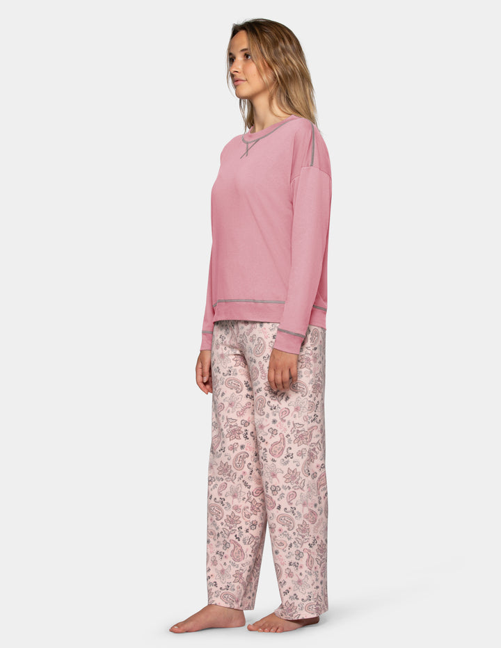A sideview of a model wearing a pink long sleeve pajama top and patterned pajama pants photographed against a light grey background.