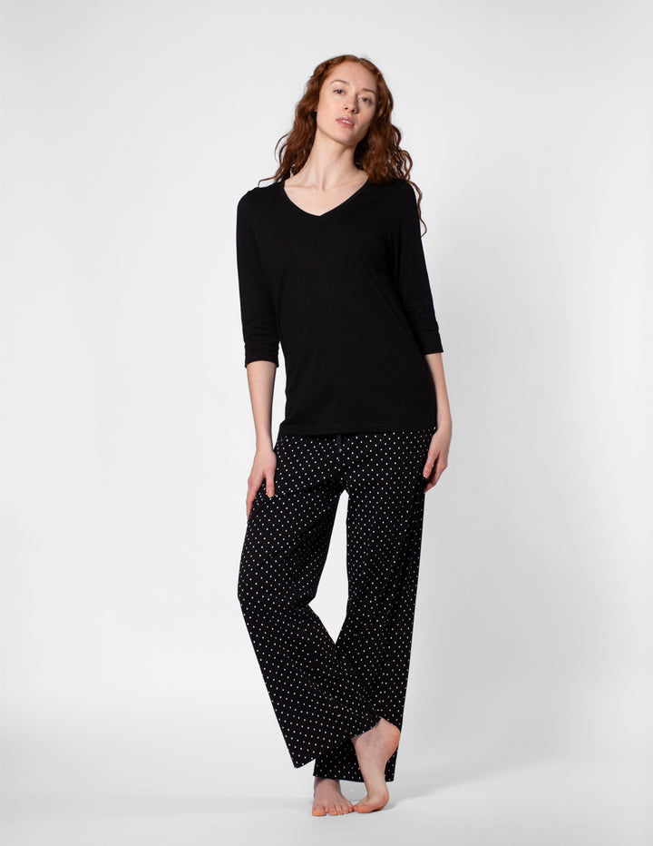 Woman wearing a black long-sleeve top and black polka dot pants on a white background