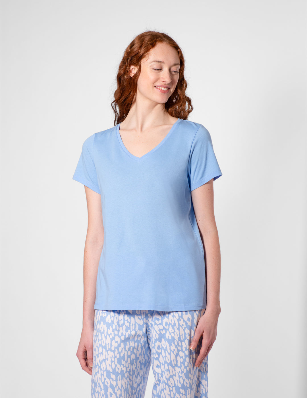 Woman wearing a light blue t-shirt and patterned pants on a white background