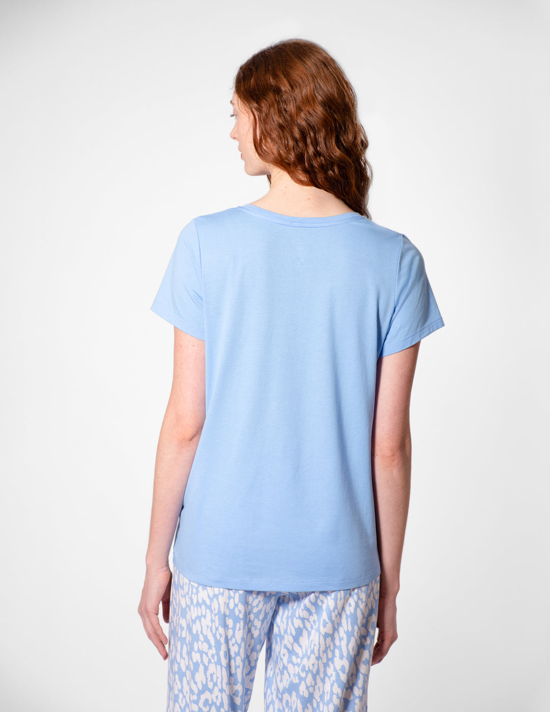 Person wearing a light blue t-shirt and patterned pants on a white background