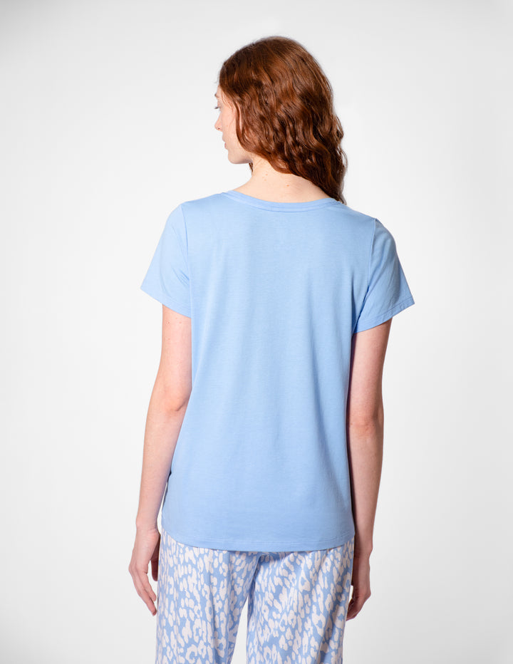 Person wearing a light blue t-shirt and patterned pants on a white background