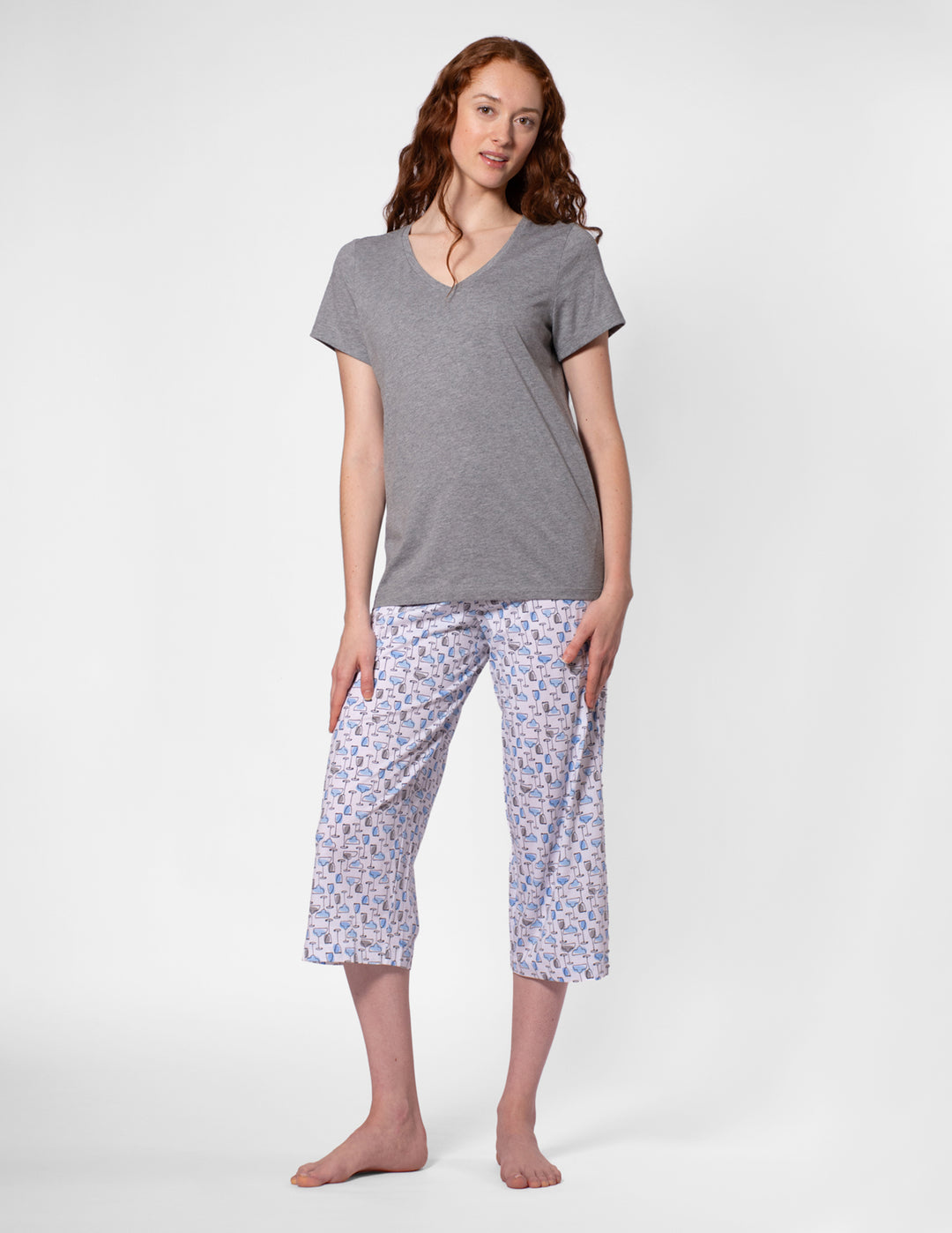 Woman wearing a gray top and patterned capri pants on a white background
