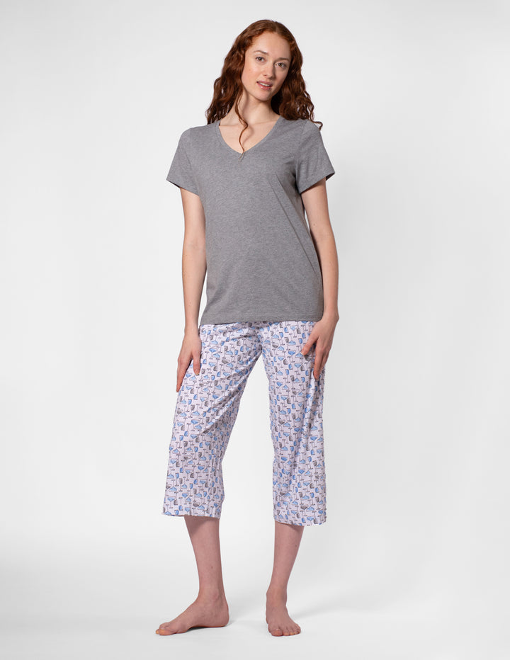 Woman wearing a gray top and patterned capri pants on a white background