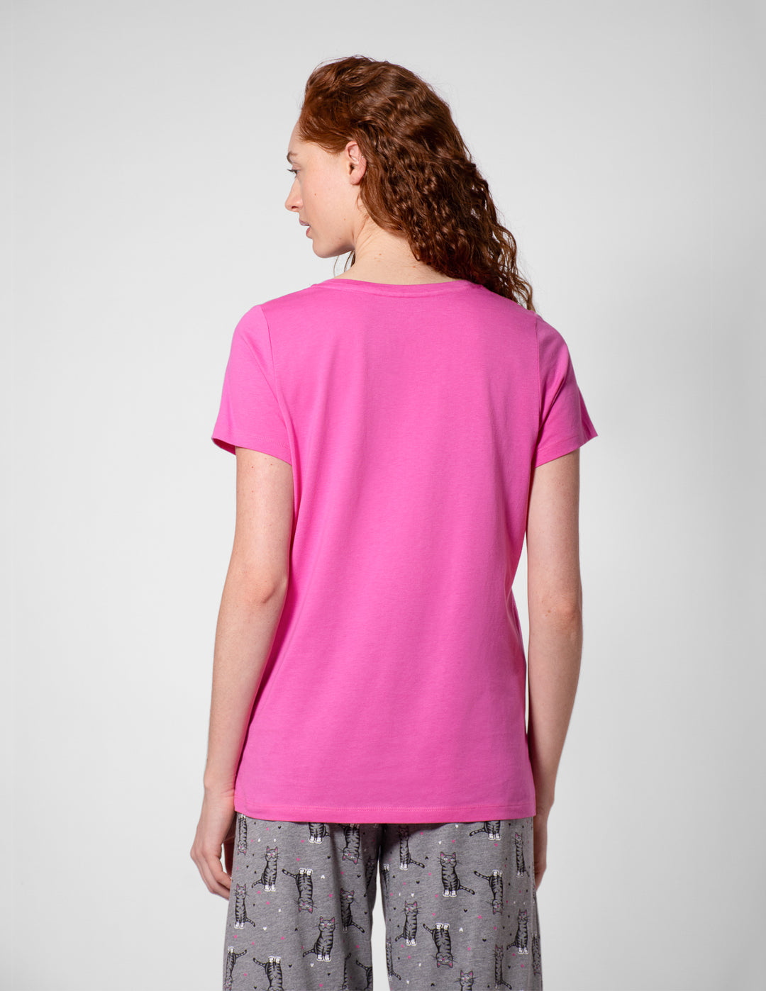 Person wearing a bright pink t-shirt and gray patterned pants on a white background