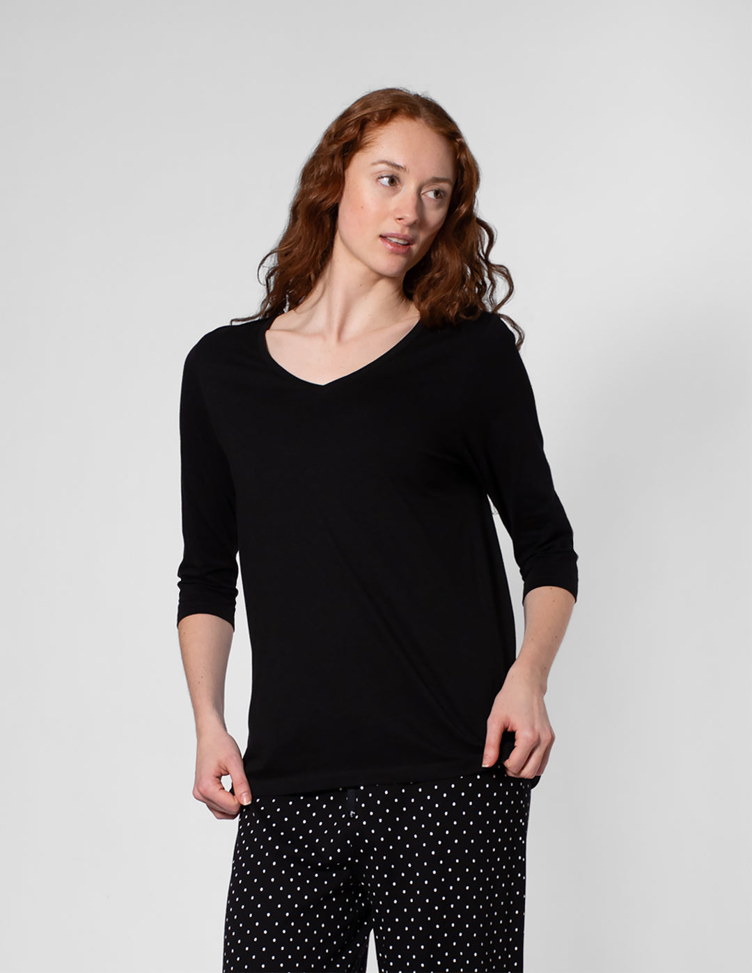 Woman wearing a black long-sleeve top and black pants with white polka dots on a light gray background