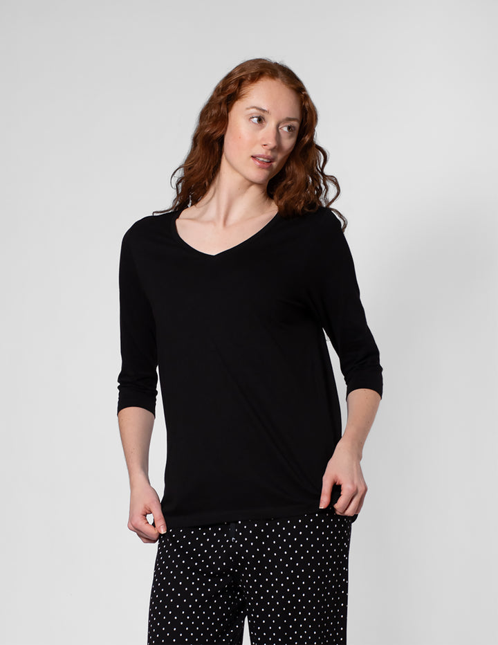 Woman wearing a black long-sleeve top and black pants with white polka dots on a light gray background