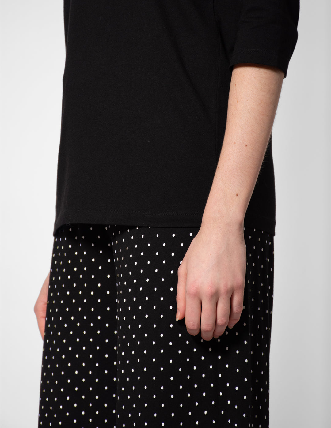Person wearing a black top and black skirt with white polka dots on a plain background