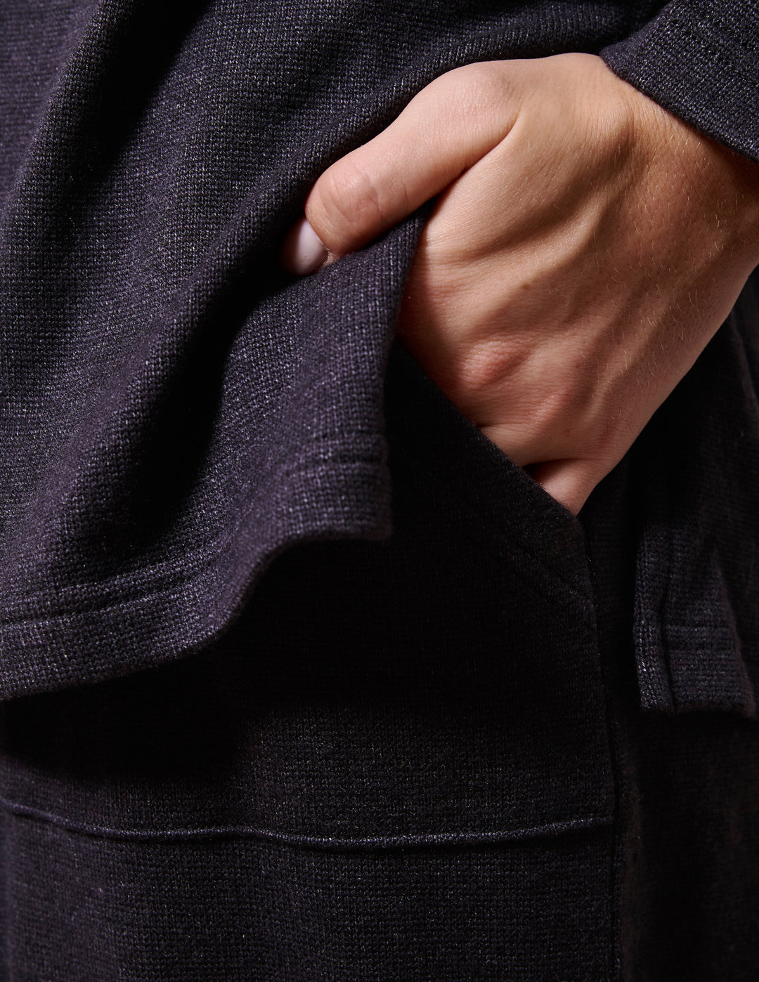 Close-up of a hand adjusting a dark grey garment with a textured fabric.