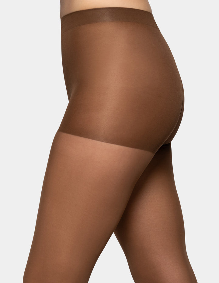 Close-up side view of a model wearing sheer brown hosiery with a wide waistband and a lighter sheer band near the upper thigh, against a light gray background.