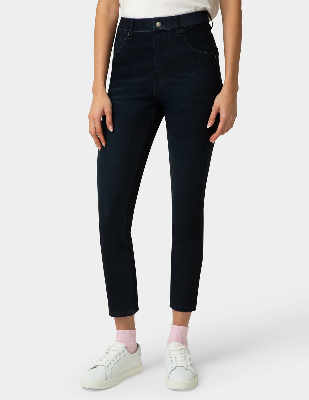 Person wearing dark blue jeans and white sneakers on a white background