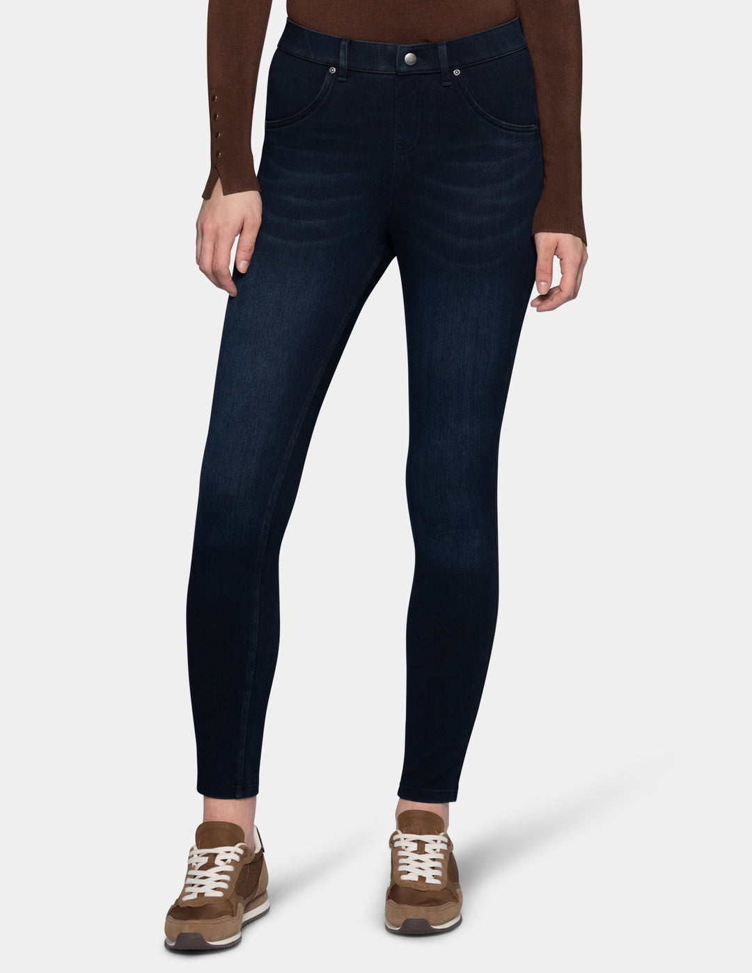 A model wearing dark blue leggings paired with a long sleeve brown top and sneakers.