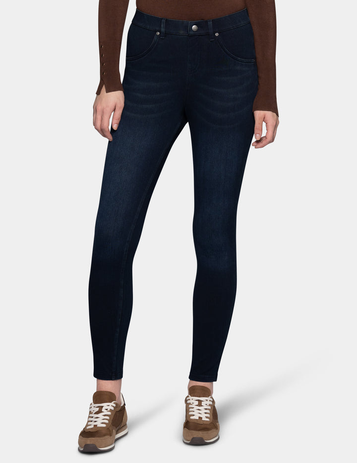 A model wearing dark blue leggings paired with a long sleeve brown top and sneakers.