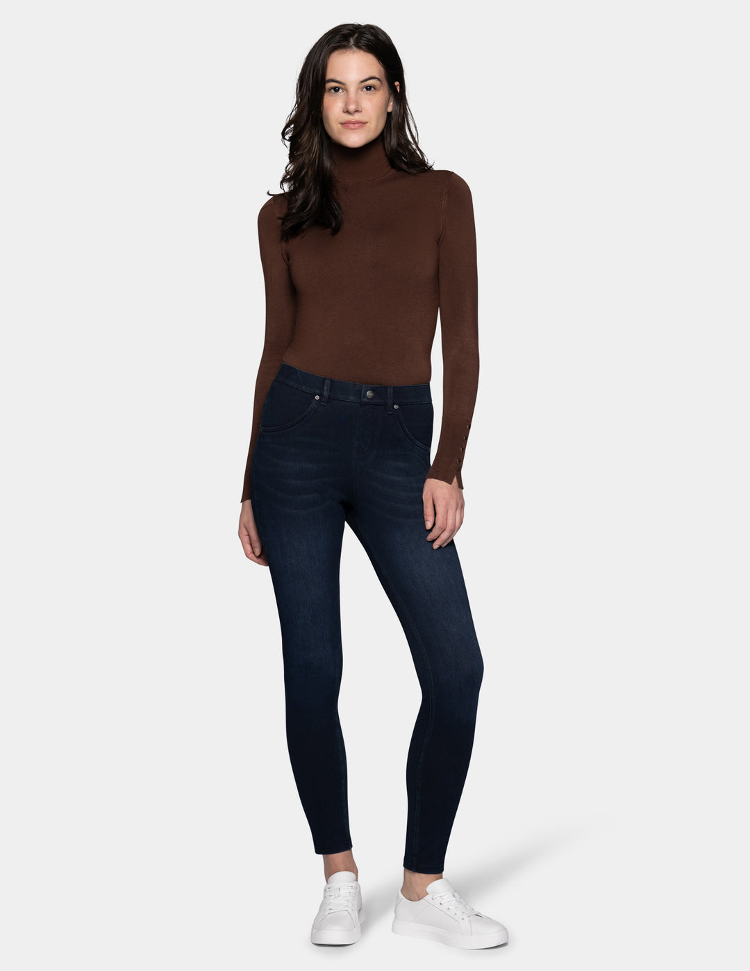 A model wearing dark blue leggings paired with a long sleeve brown top and sneakers.