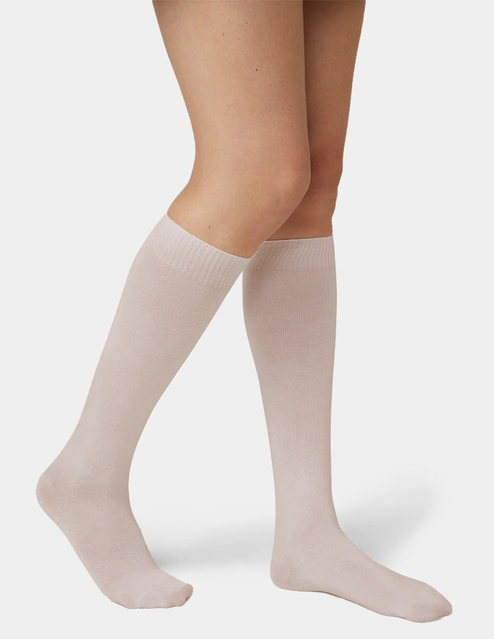 A model wearing beige knee high socks photographed against a light grey background.