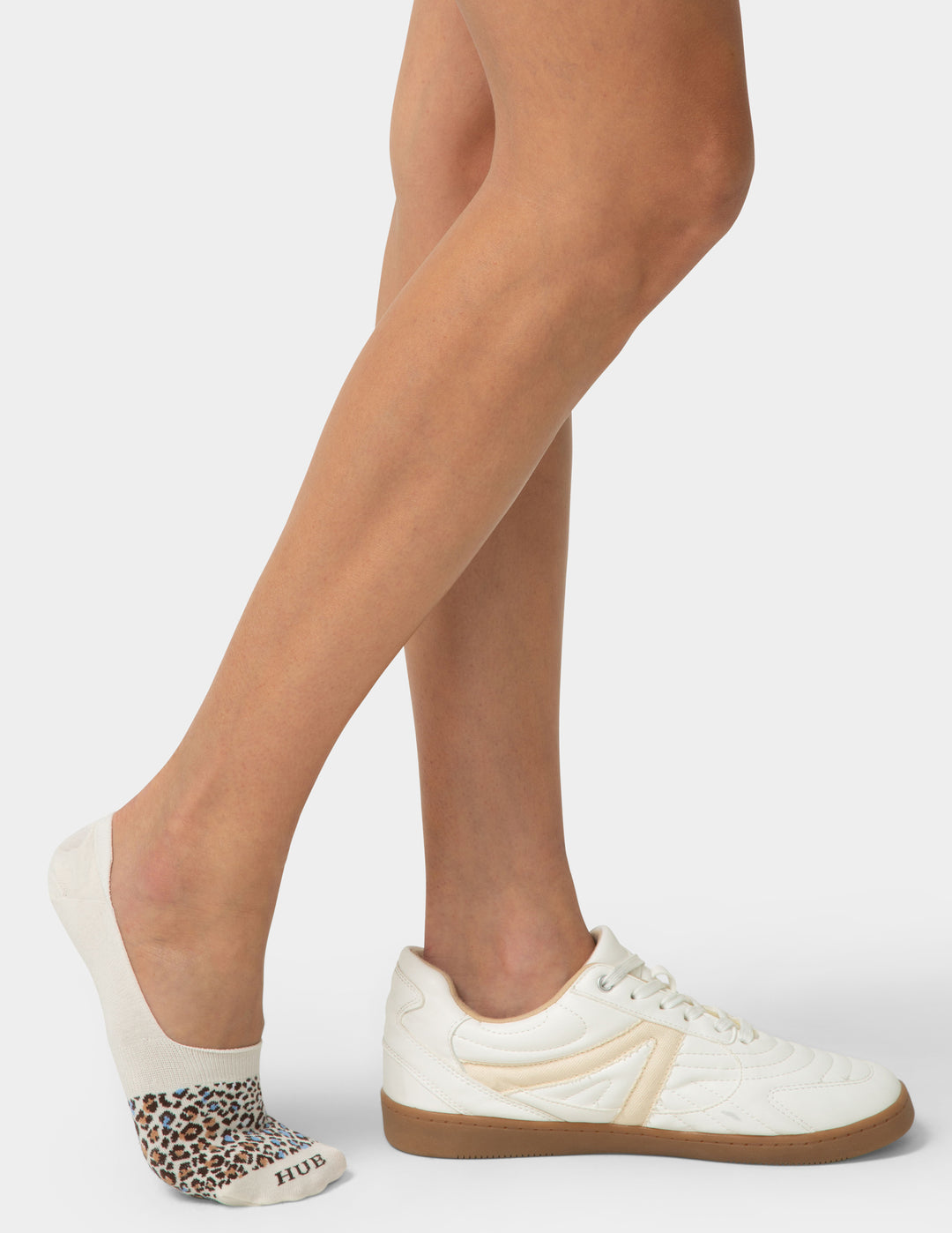 Person wearing white sneakers with leopard print socks on a plain background