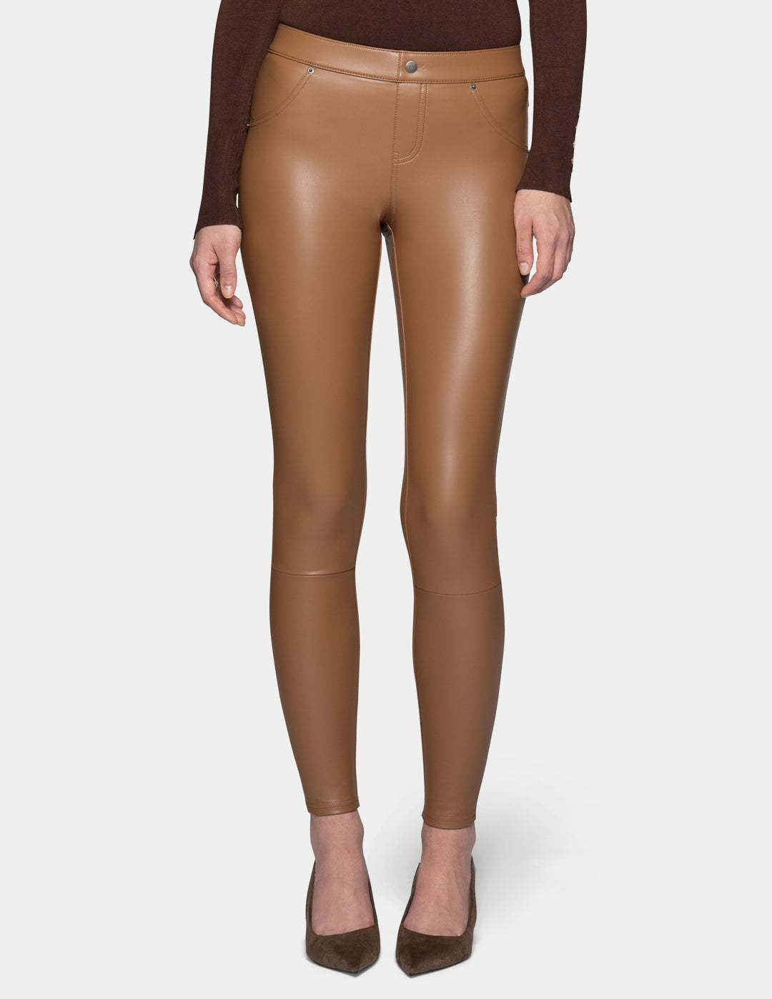 A model wearing tan faux leather leggings and a long sleeve brown top, paired with suede brown heels against a light grey background.