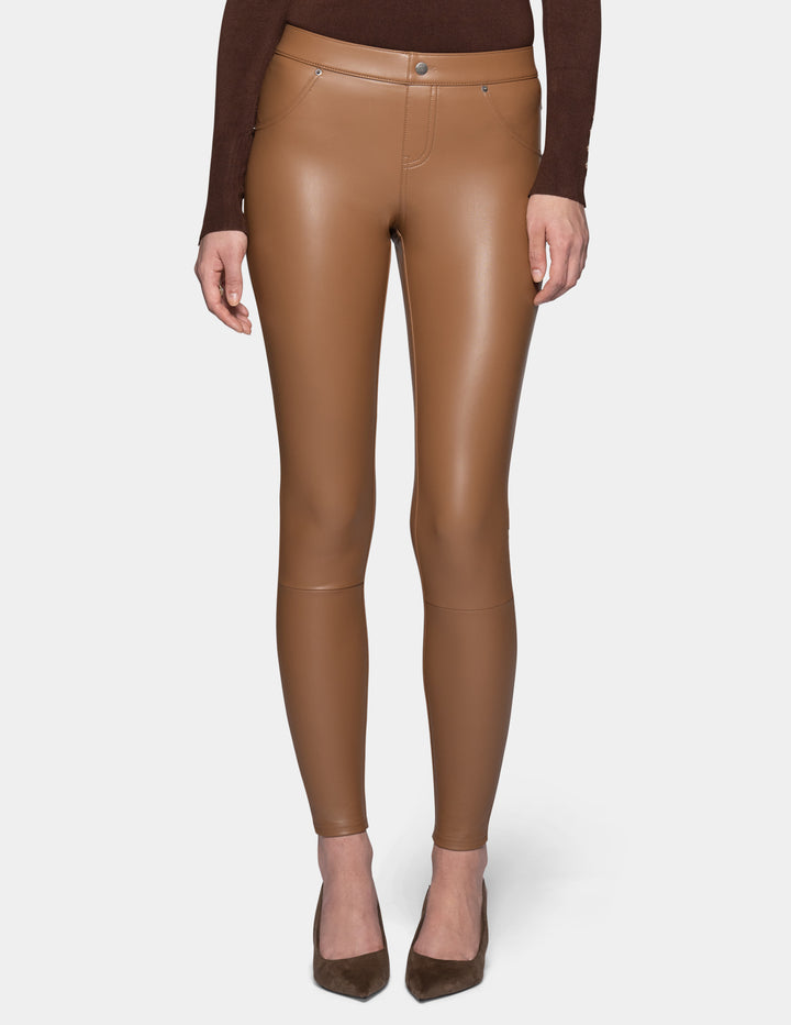 A model wearing tan faux leather leggings and a long sleeve brown top, paired with suede brown heels against a light grey background.