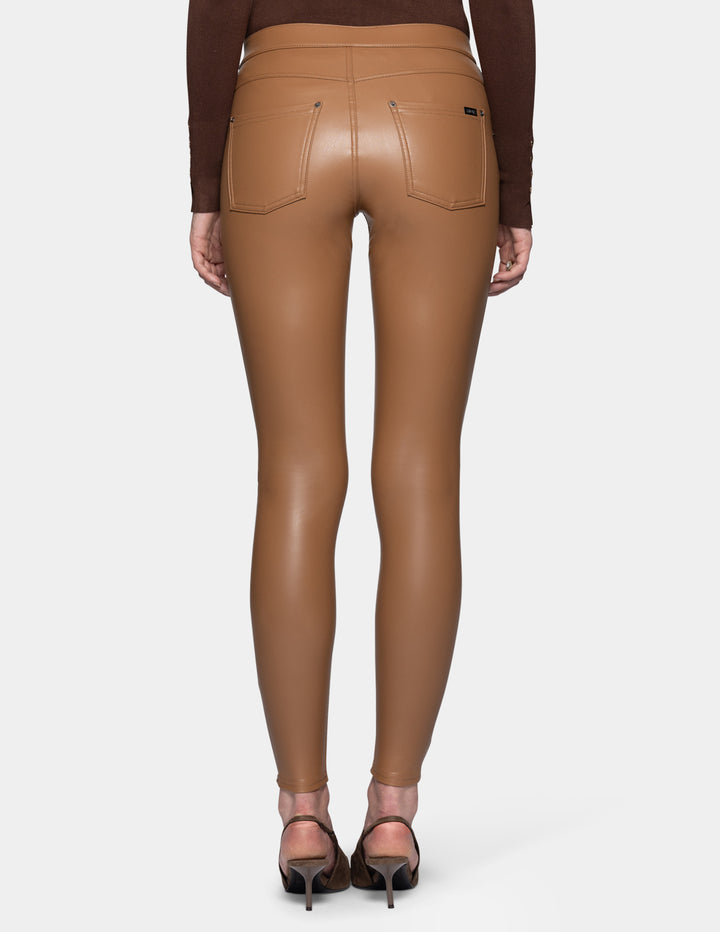 A backside view of a model wearing tan faux leather leggings and a long sleeve brown top, paired with suede brown heels against a light grey background.
