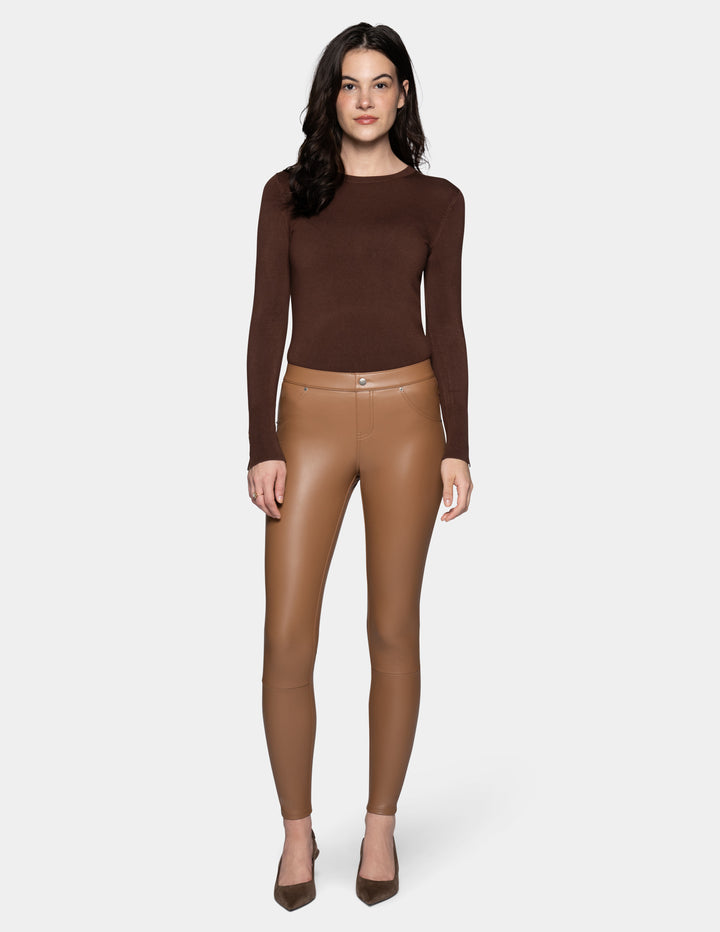 A model wearing tan faux leather leggings and a long sleeve brown top, paired with suede brown heels against a light grey background.