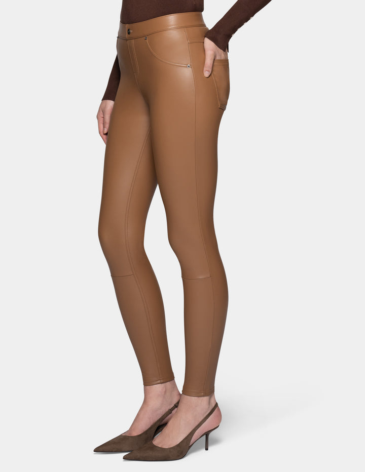 A sideview of a model wearing tan faux leather leggings and a long sleeve brown top, paired with suede brown heels against a light grey background.
