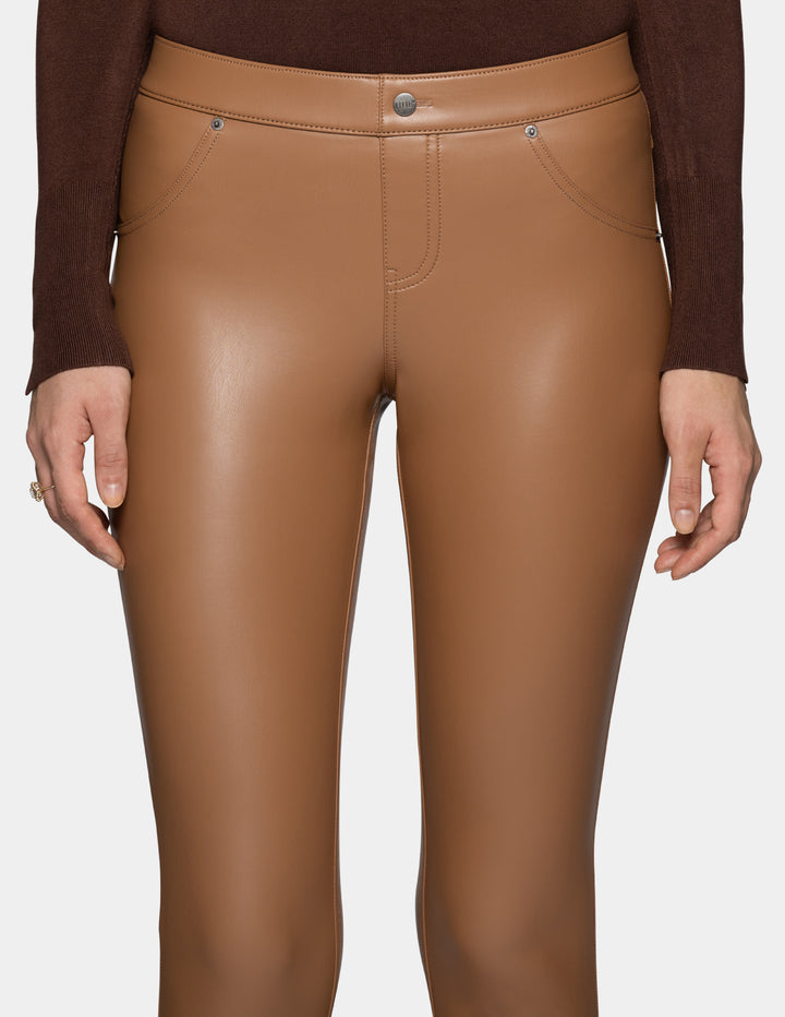 A close-up view of a model wearing tan faux leather leggings and a long sleeve brown top, against a light grey background.