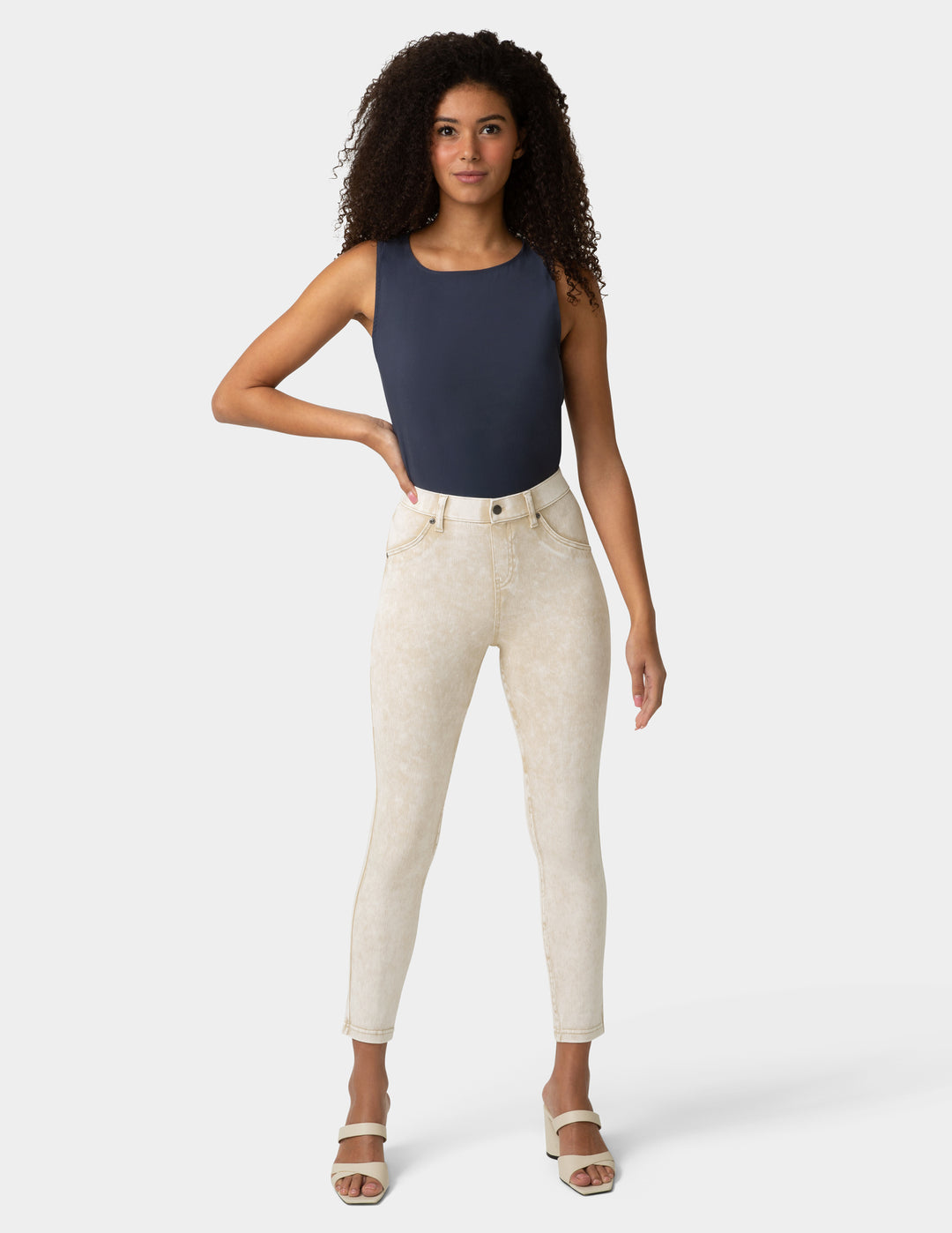 Woman wearing a navy sleeveless top and white pants on a white background