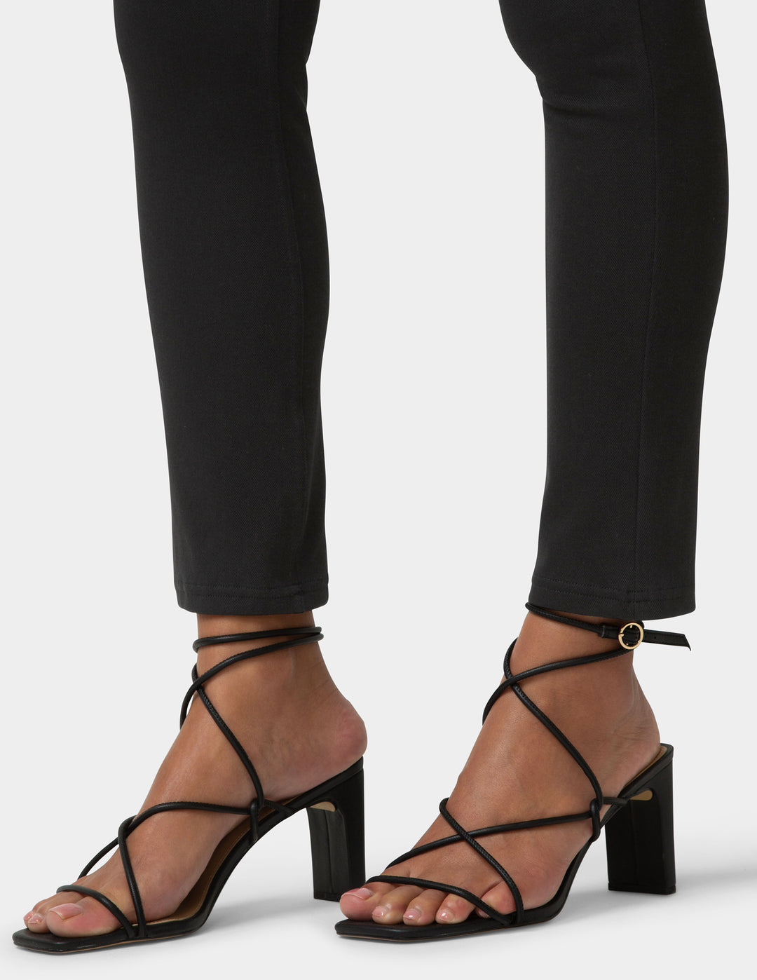 Black strappy high-heeled sandals worn with black pants on a white background