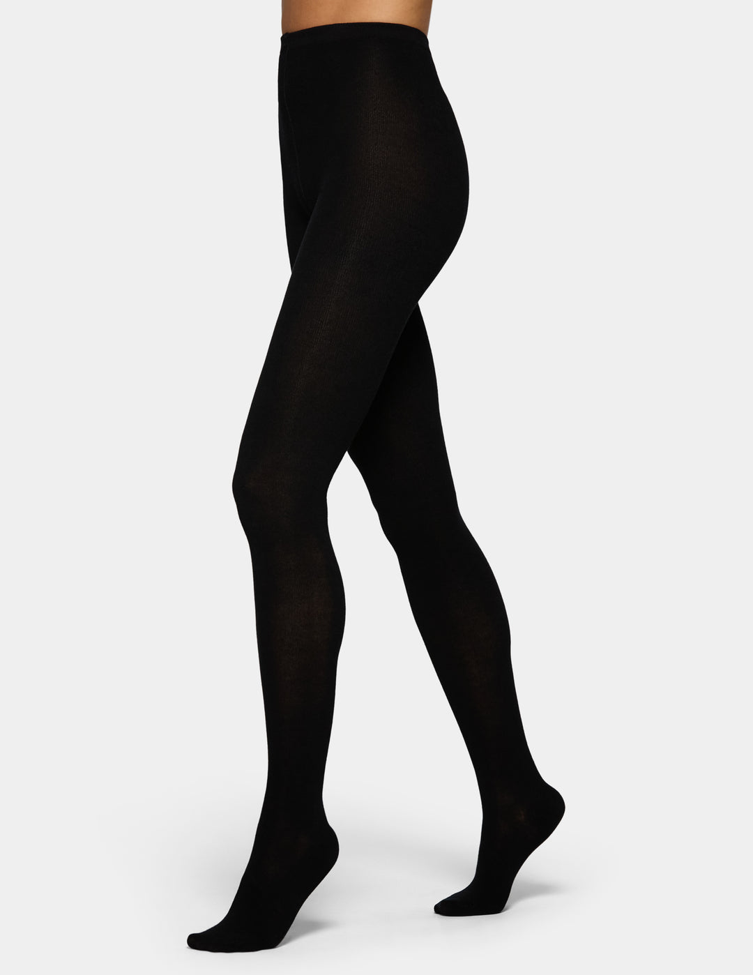 Black tights worn by a model, shown from the waist down in a side profile against a light gray studio background.