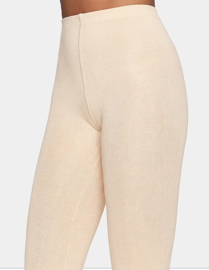 Close-up of a person wearing ribbed knit leggings in a light cream or off-white shade, shown from the waist down against a plain light gray background.