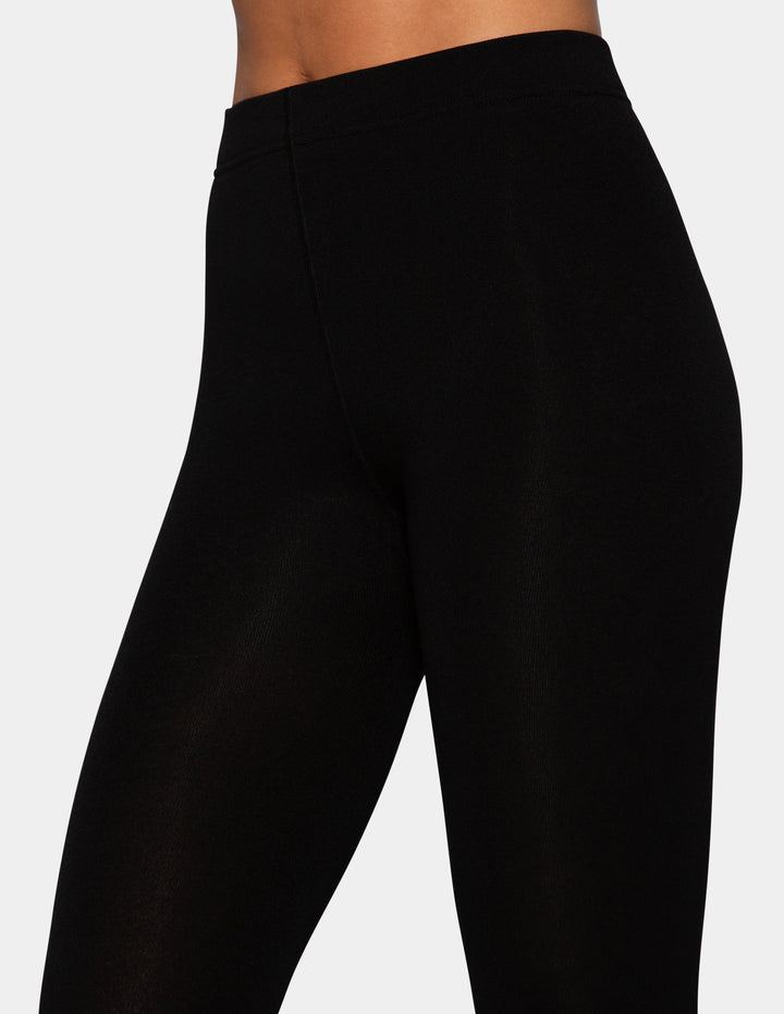 A close-up of a model wearing black tights photographed against a light gray background.