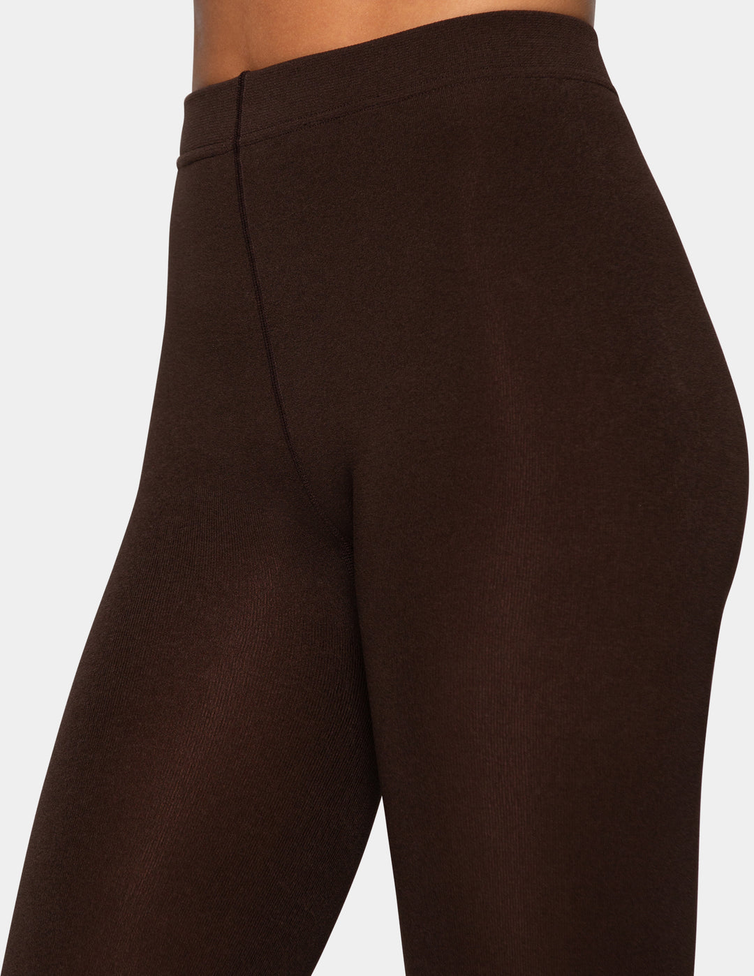 A close-up of a model wearing brown tights photographed against a light gray background.