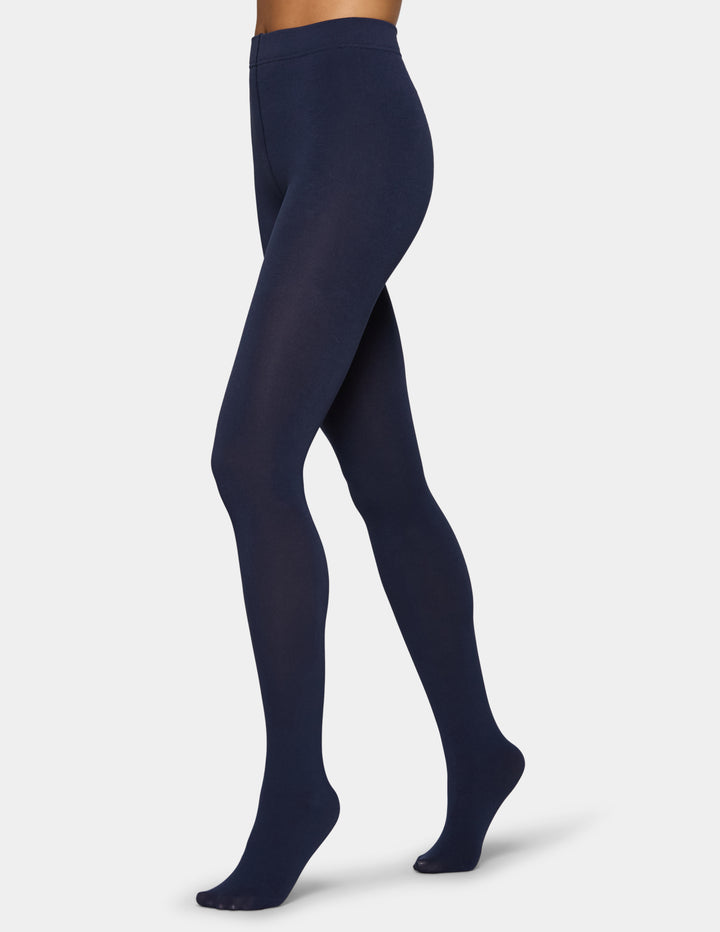 A model wearing navy tights photographed against a light gray background.