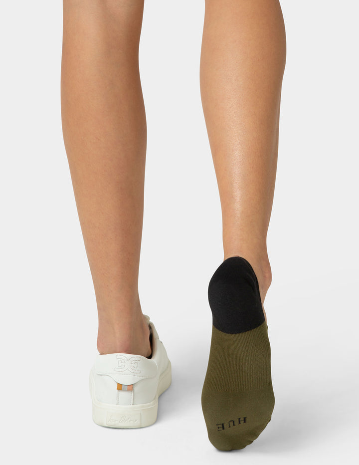 Person wearing olive green socks with white shoes on a light gray background