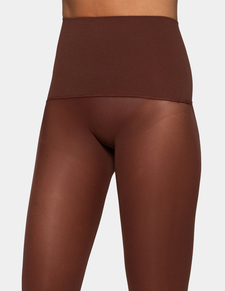 A close-up of a model wearing high-waisted, opaque brown leggings against a light gray background.