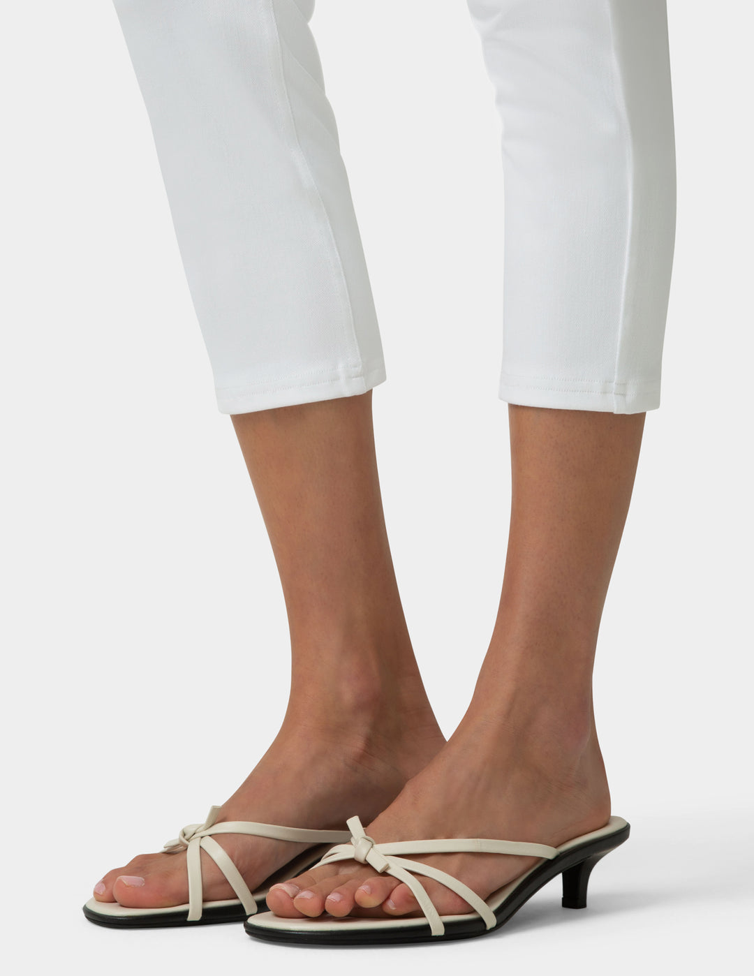 Beige strappy sandals worn with white pants on a neutral background