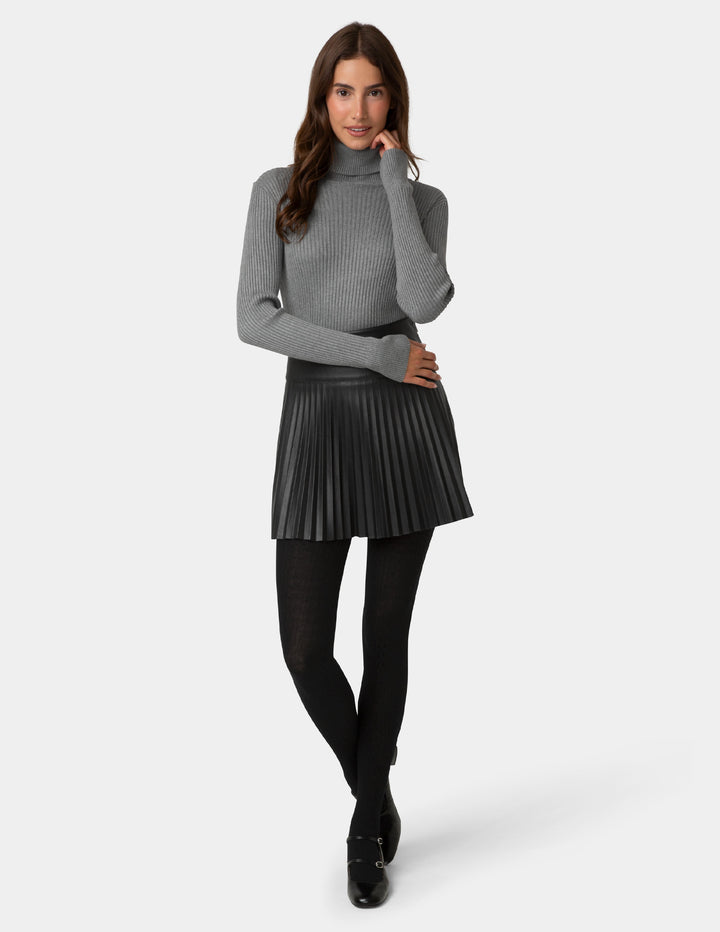 Woman wearing a gray turtleneck sweater and black pleated skirt on a white background