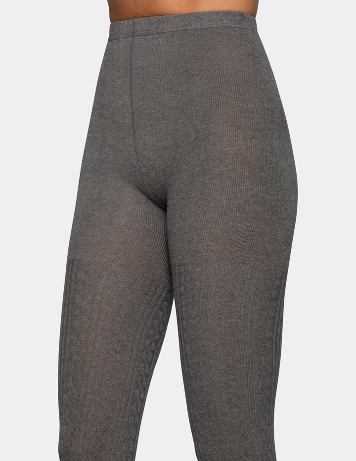 A close-up of a model wearing grey tights from the waist down against a light grey background