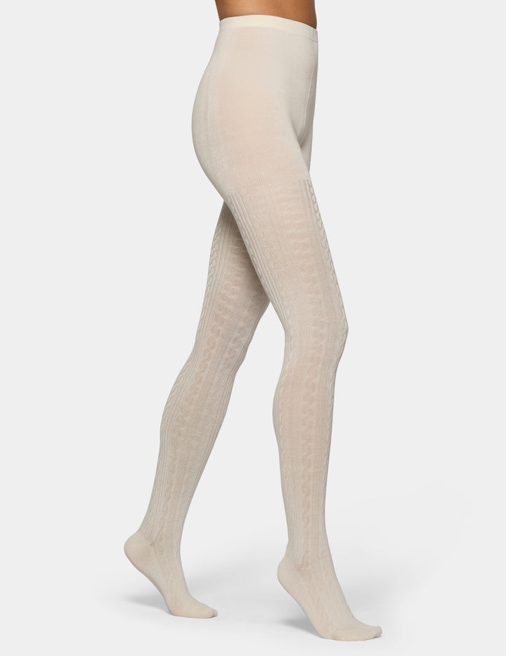 A model's legs wearing cream-colored, textured tights against a light gray studio background.
