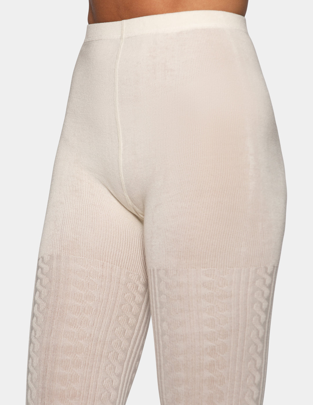 Close-up of a model wearing high-waisted cream-colored tights with textured knit patterns on the lower legs, shown from a side angle against a light gray background.